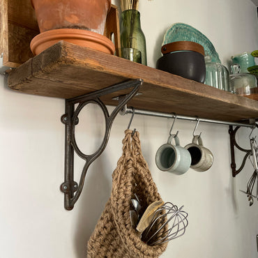 Image showing kitchen shelf with hanging storage bag suspended by a metal hook with handmade storage bag containing kitchen utensils, Jute hanging storage bag holing with whisk and ladle, handmade sustainable crochet decor, rustic natural organic homeware accessories, brown strong jute storage solution, kitchen bathroom bedroom hanging storage bag