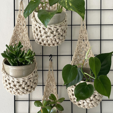 Image showing four cream wall mounted planters hanging together in a group, each one containing a pots and plant. Handmade cotton crochet plant baskets, used to display houseplants creatively in your home.