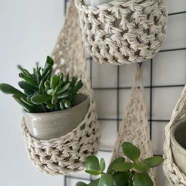 Image showing zoomed in details of four cream wall mounted planters hanging together in a group, each one containing a pots and plant. Handmade cotton crochet plant baskets, used to display houseplants creatively in your home.