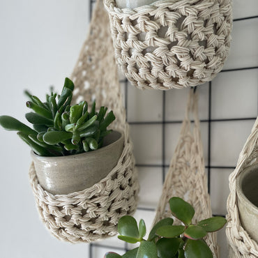 Image showing zoomed in details of four cream wall mounted planters hanging together in a group, each one containing a pots and plant. Handmade cotton crochet plant baskets, used to display houseplants creatively in your home. 