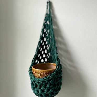 Image showing handmade green wall planter suspended against a white wall showing the tierdrop shape with pot only from small nail in the wall