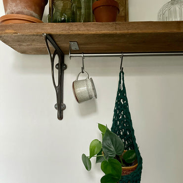 Image showing green cotton crochet hanging wall planter suspened by a hook on a rail, handmade hanging plant basket holding pot and plant hanging from hook from a rail