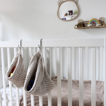 Photo showing white cotton small and large scandi storage bag in a childrens room hanging from the side of a bed from a small hook, storage bags are filled with childrens toys , space saving hanging room organiser