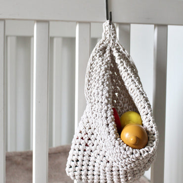 Photo showing white cotton small scandi storage bag in a childrens room hanging from the side of a bed from a small hook, storage bags are filled with childrens toys , space saving hanging room organiser