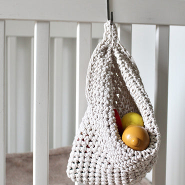  Photo showing white cotton small scandi storage bag in a childrens room hanging from the side of a bed from a small hook, storage bags are filled with childrens toys , space saving hanging room organiser