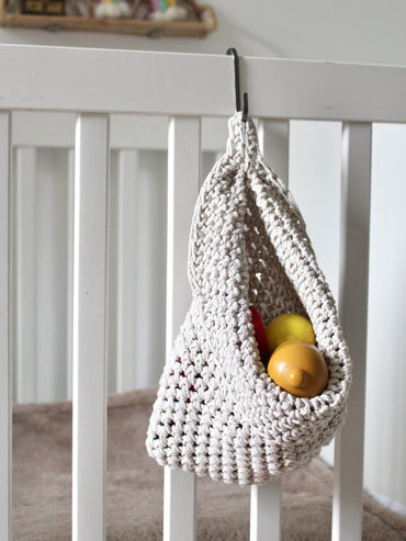  Photo showing white cotton small scandi storage bag in a childrens room hanging from the side of a bed from a small hook, storage bags are filled with childrens toys , space saving hanging room organiser