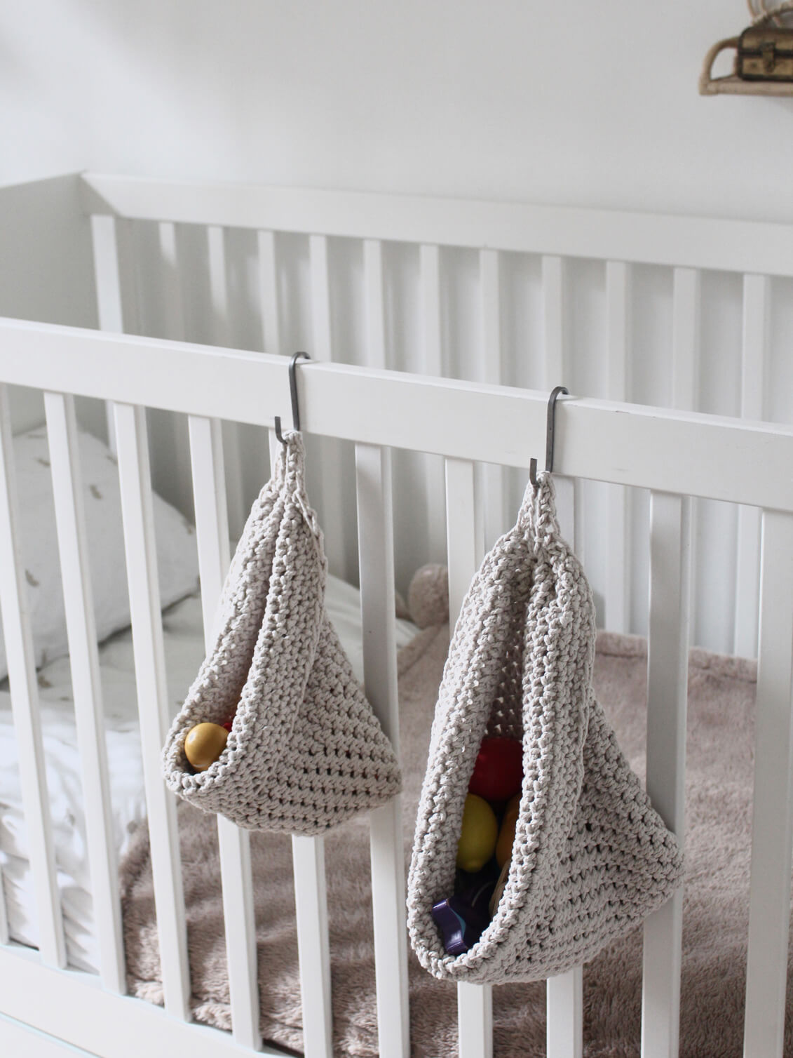  Photo showing white cotton small and large scandi storage bag in a childrens room hanging from the side of a bed from a small hook, storage bags are filled with childrens toys , space saving hanging room organiser
