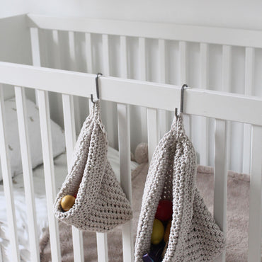 Photo showing white cotton small and large scandi storage bag in a childrens room hanging from the side of a bed from a small hook, storage bags are filled with childrens toys , space saving hanging room organiser