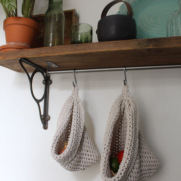 Photo showing white cotton small and large scandi storage bags in a kitchen suspended by metal hooks from a hanging shelf, the space saving storage bags are filled with fruits and vegetables
