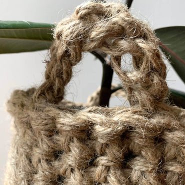 Close up view of crocheted plant basket handles. Shows the texture and curved shaped of the handle attached to basket. Showing natural jute texture and brown colour of basket.