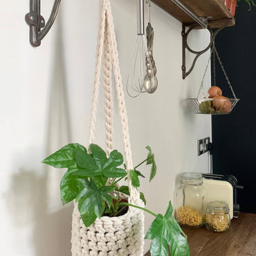 Indoor cream cotton hanging plant holder with three long crocheted straps, finished with a loop to hang up. Image shows planter hanging in a kitchen, from a hanging rail, with a pot and plant inside. Made with recycled cotton cord.