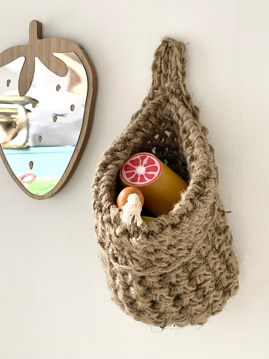small jute space saving storage bag hanging in a childrens bedroom to orgaanise toys, picture showing a small mirror and storage bag hanging beside eachother, handmade hanging storage bag holding childrens toys