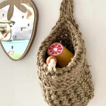 small jute space saving storage bag hanging in a childrens bedroom to orgaanise toys, picture showing a small mirror and storage bag hanging beside eachother, handmade hanging storage bag holding childrens toys