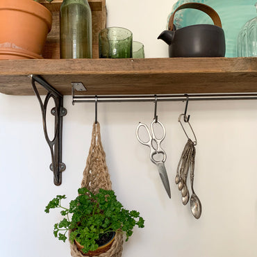 Photo showing small jute hanging planter in a kitchen, holding a ceramic pot and parsely plant. Planter is hanging from a metal hook attached from a metal rail. 