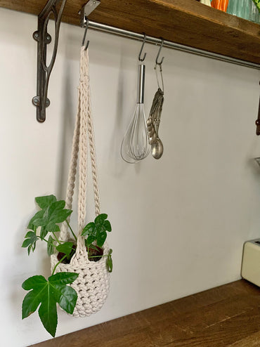 Indoor cream cotton hanging plant holder with three long crocheted straps, finished with a loop to hang up. Image shows planter hanging in a kitchen, from a hanging rail, with a pot and plant inside. Made with recycled cotton cord.