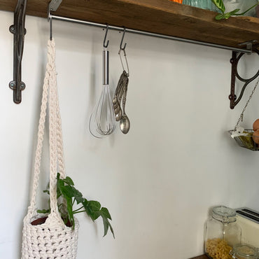 Indoor cream cotton hanging plant holder with three long crocheted straps, finished with a loop to hang up. Image shows planter hanging in a kitchen, from a hanging rail, with a pot and plant inside. Made with recycled cotton cord.