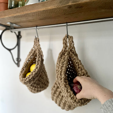 mage showing kitchen shelf with hanging storage bag suspended by a metal hook, handmade storage bag containing red onions in a kitchen, breathable storage bag for kitchen produce displayed on a hanging rail, space saving hanging storage in a kitchen wall, brown jute handmade storage bag