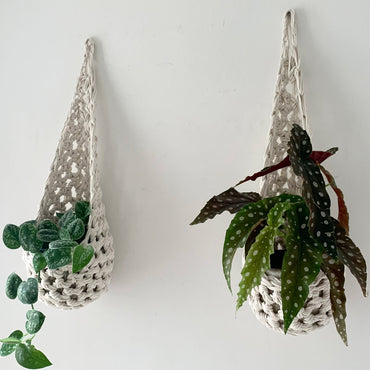 Image of two white cotton crochet hanging wall planter against a wall of a bedroom. The photo shows the planter with a pot and plant inside it, in order to demonstate tierdrop shape of design. Hanging by a small nail in the wall.