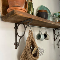 Image showing kitchen shelf with hanging storage bag suspended by a metal hook with handmade storage bag containing kitchen utensils, Jute hanging storage bag holing with whisk and ladle, handmade sustainable crochet decor, rustic natural organic homeware accessories, brown strong jute storage solution, kitchen bathroom bedroom hanging storage bag