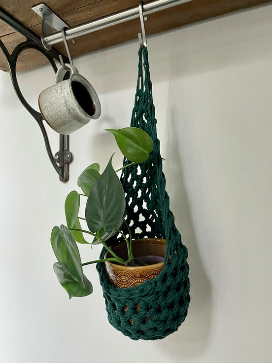 Image showing green cotton crochet hanging wall planter suspened by a hook on a rail, handmade hanging plant basket holding pot and plant hanging from hook from a rail