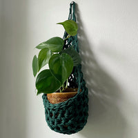 Image showing handmade green wall planter suspended against a white wall showing the tierdrop shape with pot and trailing plant from small nail in the wall