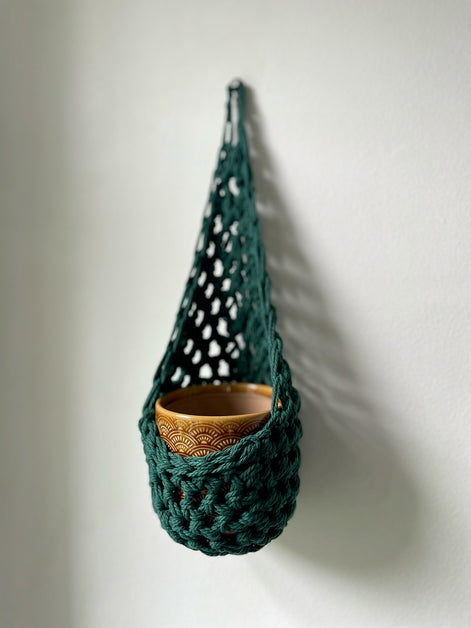 Image showing handmade green wall planter suspended against a white wall showing the tierdrop shape with pot only from small nail in the wall 