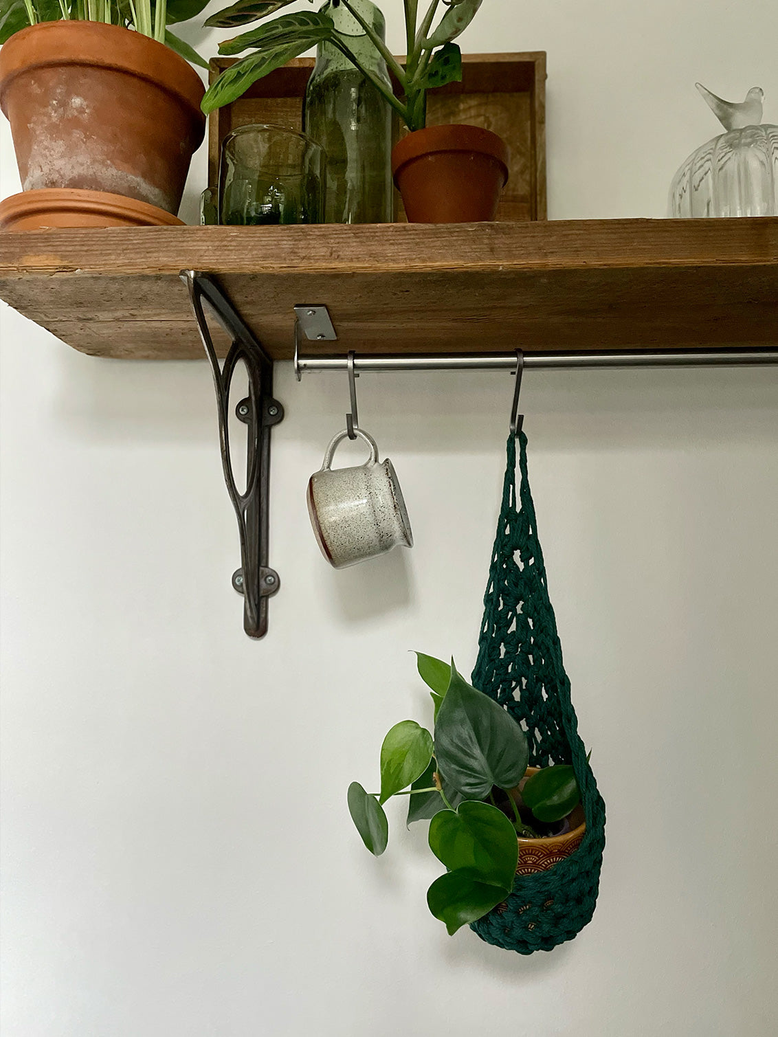 Image showing green cotton crochet hanging wall planter suspened by a hook on a rail, handmade hanging plant basket holding pot and plant hanging from hook from a rail