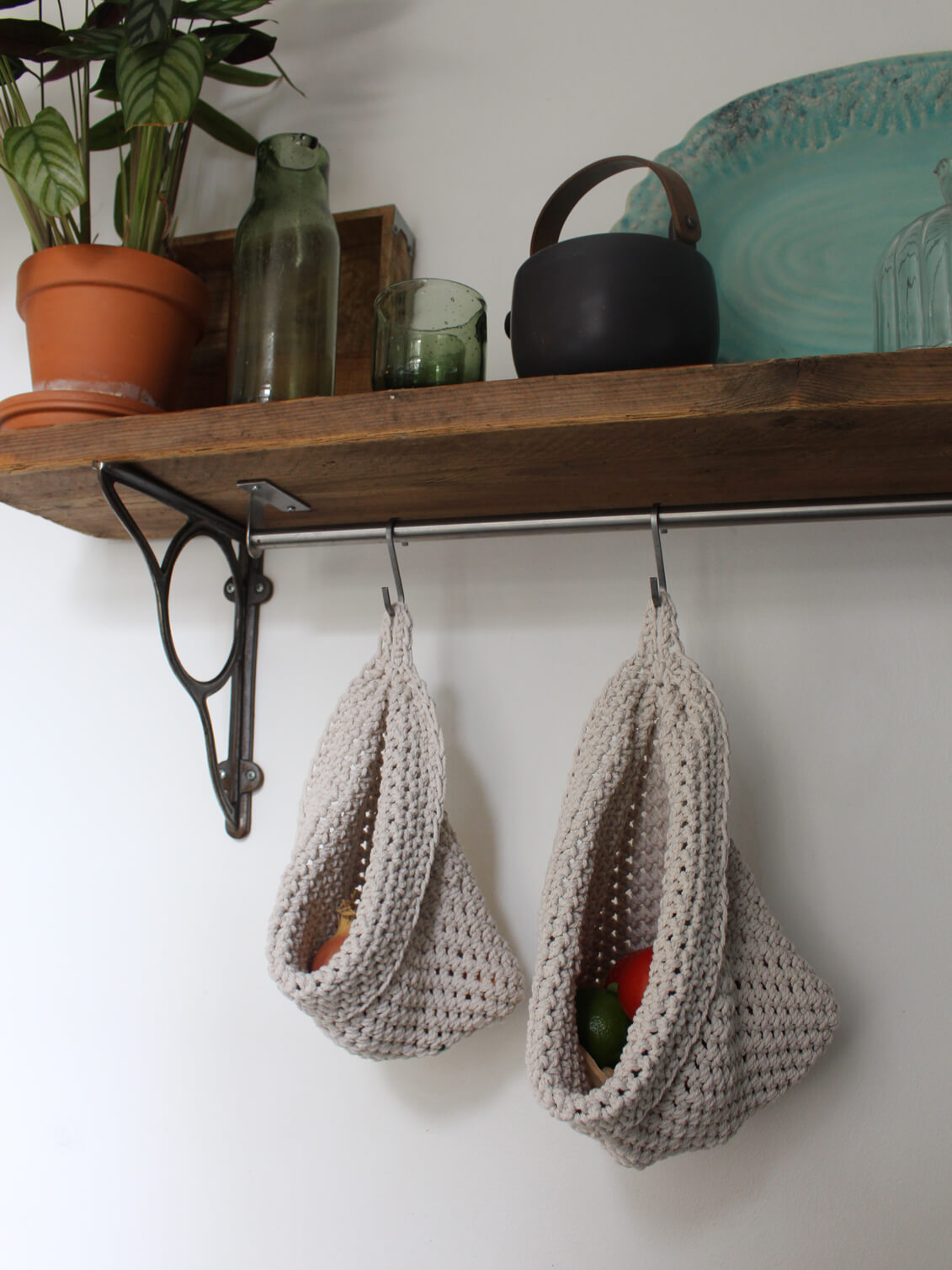 Photo showing white cotton small and large scandi storage bags in a kitchen suspended by metal hooks from a hanging shelf, the space saving storage bags are filled with fruits and vegetables