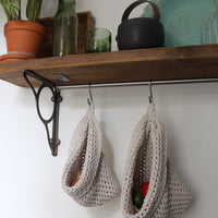 Photo showing white cotton small and large scandi storage bags in a kitchen suspended by metal hooks from a hanging shelf, the space saving storage bags are filled with fruits and vegetables
