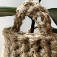Close up view of crocheted plant basket handles. Shows the texture and curved shaped of the handle attached to basket. Showing natural jute texture and brown colour of basket.