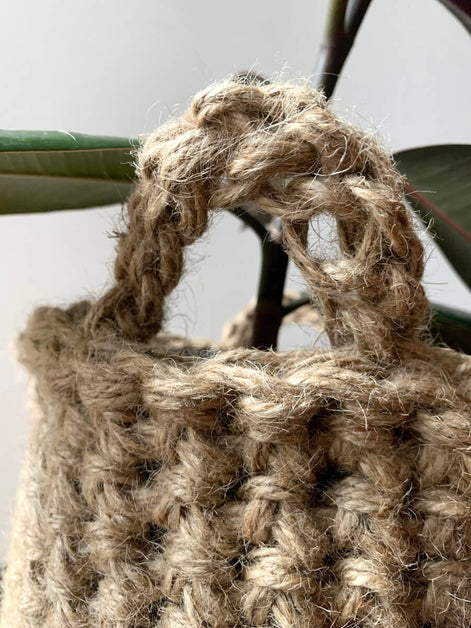 Close up view of crocheted plant basket handles. Shows the texture and curved shaped of the handle attached to basket. Showing natural jute texture and brown colour of basket.