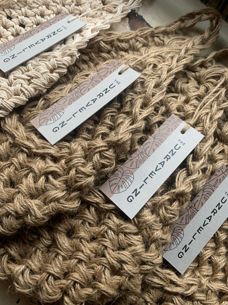 Photo showing 4 jute wall planters with swing tags, lying flat. Showing the tierdrop shape and The Unraveling branding. 