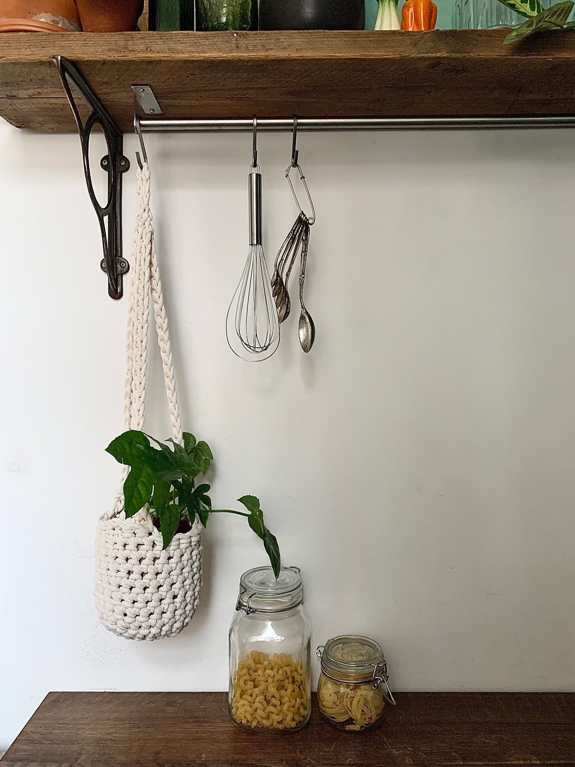 Indoor cream cotton hanging plant holder with three long crocheted straps, finished with a loop to hang up. Image shows planter hanging in a kitchen, from a hanging rail, with a pot and plant inside. Made with recycled cotton cord.