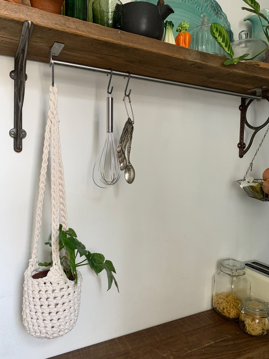 Indoor cream cotton hanging plant holder with three long crocheted straps, finished with a loop to hang up. Image shows planter hanging in a kitchen, from a hanging rail, with a pot and plant inside. Made with recycled cotton cord.