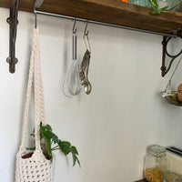 Indoor cream cotton hanging plant holder with three long crocheted straps, finished with a loop to hang up. Image shows planter hanging in a kitchen, from a hanging rail, with a pot and plant inside. Made with recycled cotton cord.